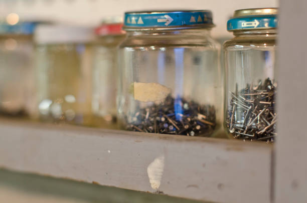 A row of wooden shelves in a old dusty work shop full of glass jars filled with junk and screws keeping everything stored.