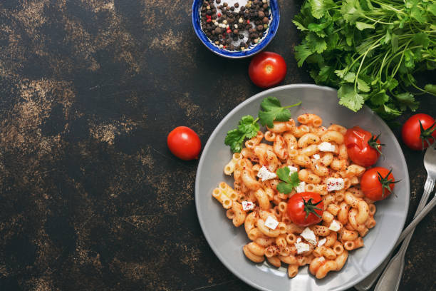 Pasta with cherry tomato sauce feta cilantro on a dark rustic background, copy space. View from above.