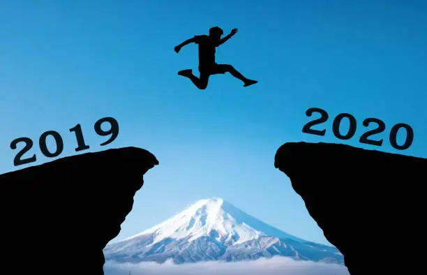 Photo of A young man jump between 2019 and 2020 years over the sun and through on the gap of hill  silhouette evening colorful sky. happy new year 2020.