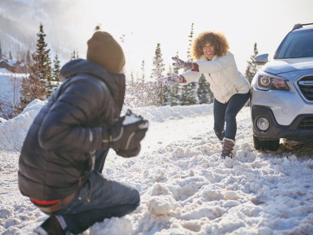 Woman standing outdoors during winter, laughing and smiling, throwing snow into the air during playful interaction with another person in a snowy forest