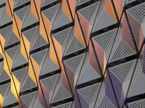 Photo of modern steel cladding with angular geometric patterns  and square holes in a shiny metallic finish with colored reflection on the wall of a car park in leeds