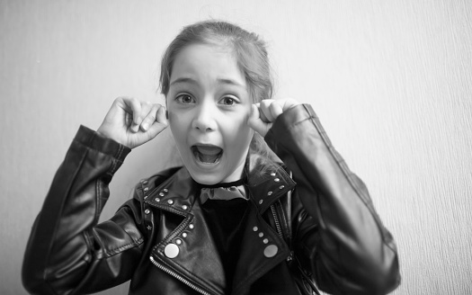 Little girl in leather jacket covers her ears with her fingers isolated