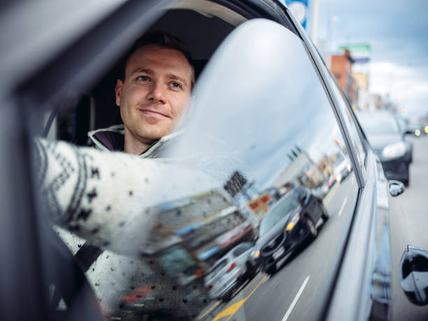 Millennial man driving in a car in winter Caucasian Millennial man driving in a car in winter. Busy downtown street with people and cars in the background. hipster car stock pictures, royalty-free photos & images