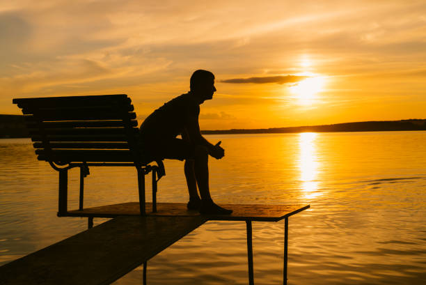 istock Single man sitting on the bench on a small bridge in the evening and looking at sunset 1088210934