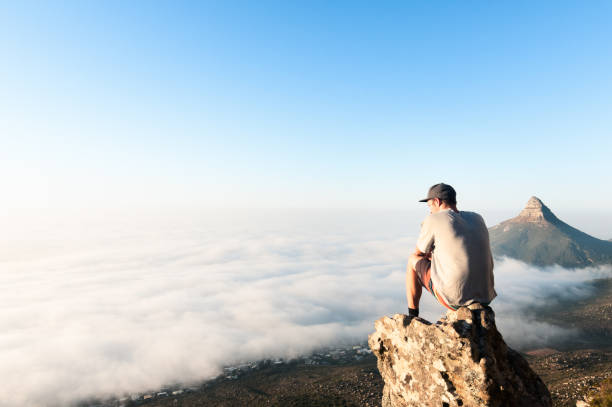 jeune homme assis sur la montagne au-dessus des nuages de cape town, south africa - clifton le cap photos et images de collection