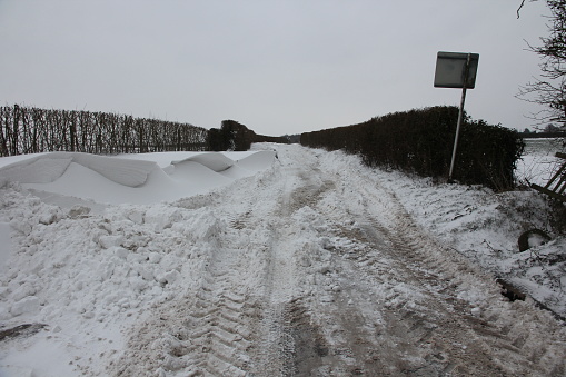 Snow slush and ice on isolated rural road in winter with tyre marks and deep snowdrifts