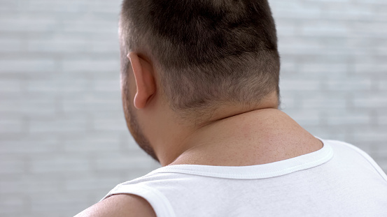 Fat man sitting hunched over, overweight person suffering from backpain, closeup