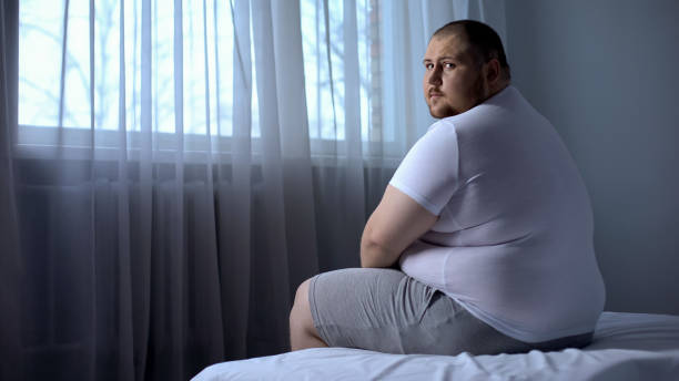 カメラ、うつ病、不安を見て、自宅のベッドの上に座っている悲しいデブ男 - men muscular build abdominal muscle large ストックフォトと画像
