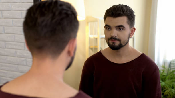 istock Depressed young male looking in mirror, smiling sadly, suffering insecurities 1088258358