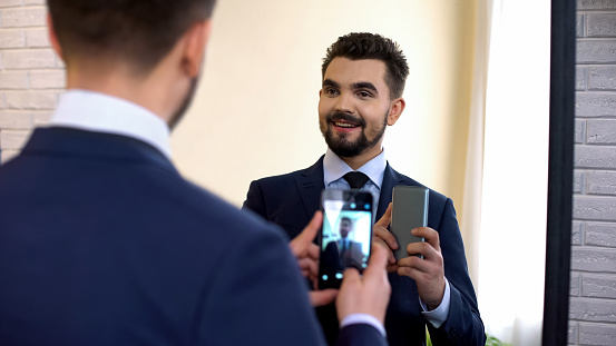 Cheerful manager in suit taking selfie in mirror reflection, social networking