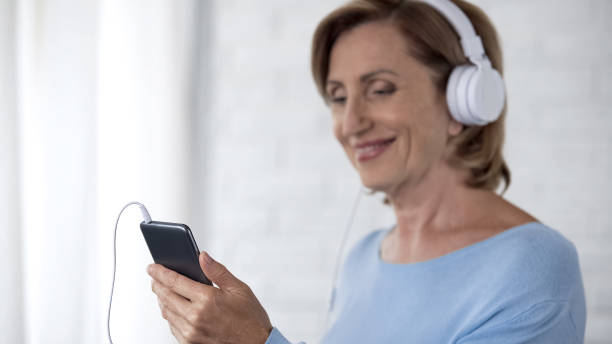 istock Aged female in headphones holding mobile phone scrolling screen, mobile app 1088258448