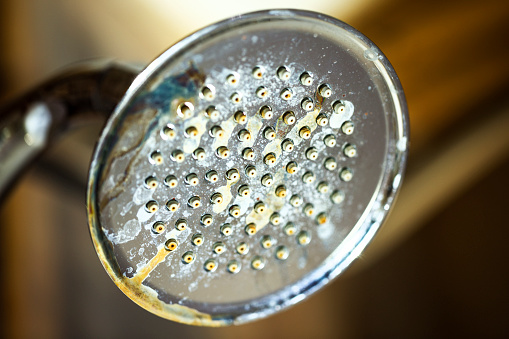 A chrome shower head with hard water deposit and rust stains.