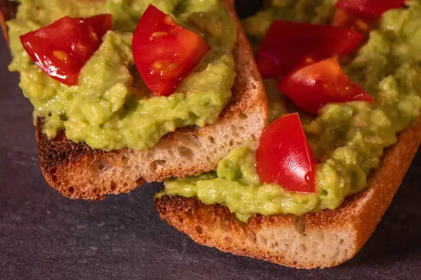 Close-up of avocado toast: guacamole, tomato, and herbs on a toasted baguette.