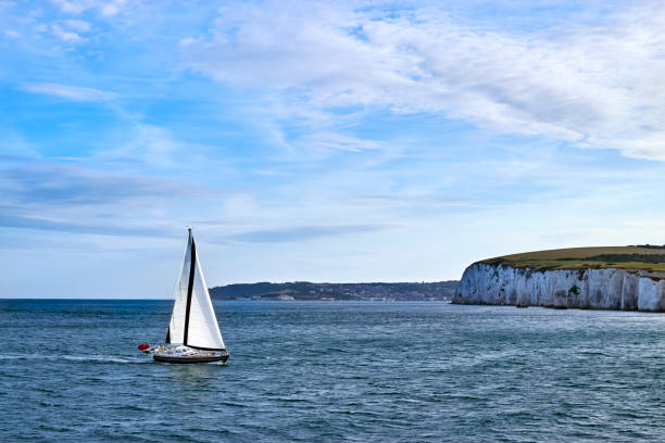 Sailing Yacht sailing in the English Channel off the white cliffs in calm water with blue sky and some cloud