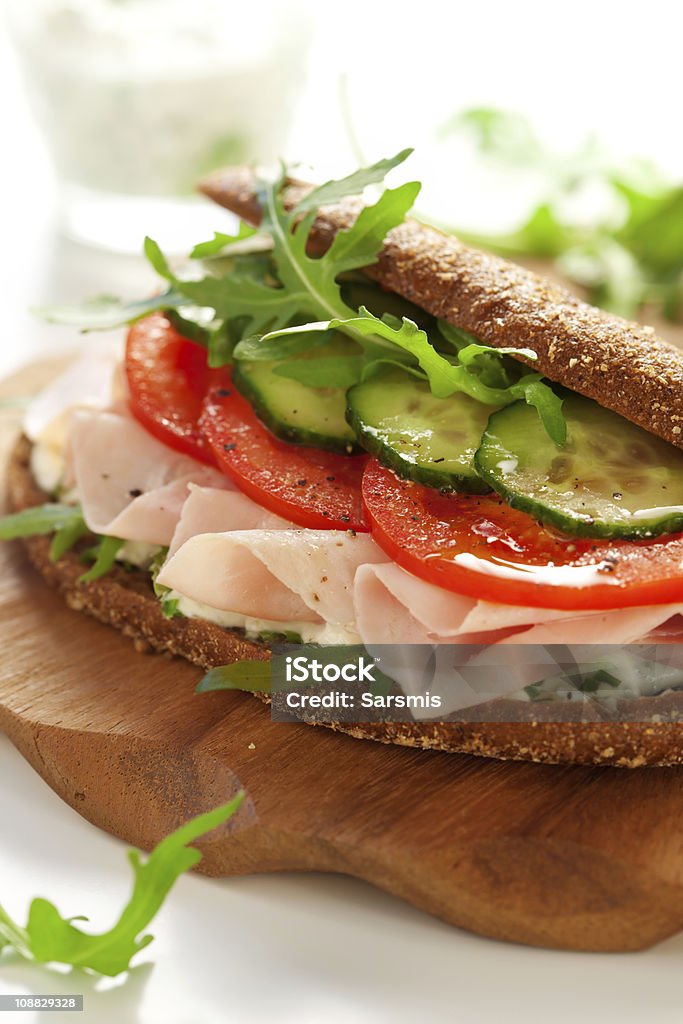 Sandwich with ham and vegetables Sandwich with ham,tomato, cucumber and arugula on the wooden cutting board Appetizer Stock Photo