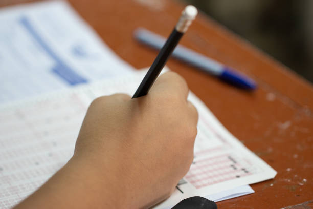 istock School Students hands taking exams, writing examination with holding pencil on optical form of standardized test with answers sheet on desk doing final exam in classroom. Education assessment Concept 1088310468