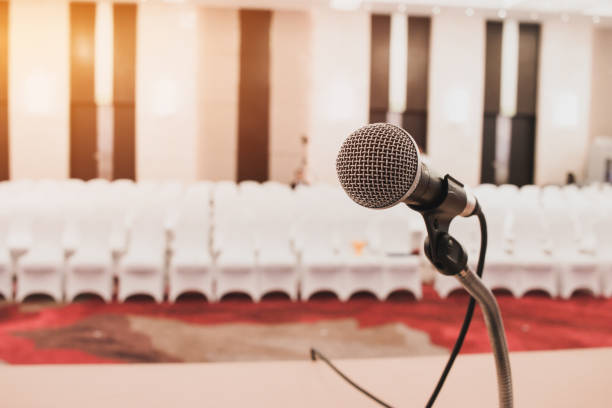 istock Microphones on abstract blurred of speech in seminar room or front speaking conference hall light, white chairs for people in event meeting convention hall in hotel. 1088310506