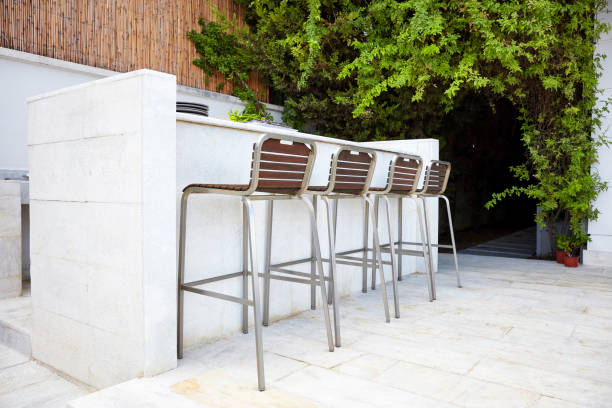 Four empty bar stool chairs with wooden seats and metal foot near a white concrete bar counter Four empty bar stool chairs with wooden seats and metal foot near a white concrete bar counter in an outdoor bar bar exterior stock pictures, royalty-free photos & images