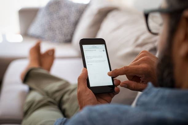 Man reading email on smartphone Closeup of a man hand holding cellphone with internet browser on screen. Man with spectacles relaxing sitting on couch while looking at mobile phone. Closeup of mature latin man using smartphone to checking email at home. house phone stock pictures, royalty-free photos & images