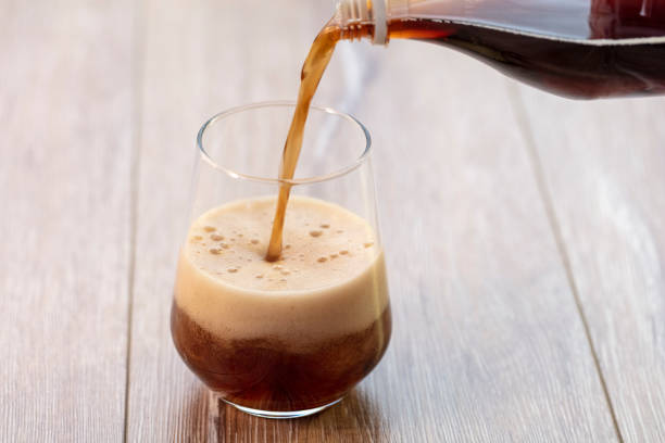 Soda (cola) being poured into plain glass with ice