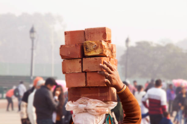 istock Image of female worker carrying bricks over her head on a construction site at crowdy public place 1088353278