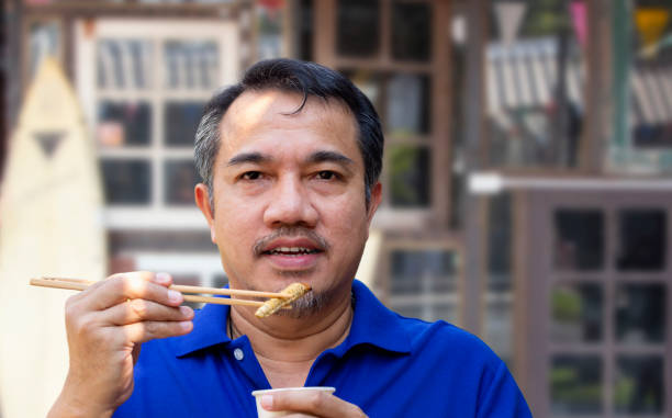 Man eating a worm, holding it in the hand. The concept of protein food sources from insects. It is a good source of protein, vitamin B12, and fiber, it is low in fat.