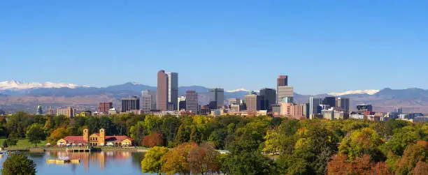 City skyline of Denver Colorado downtown with snowy Rocky Mountains and the City Park Lake. Large panorama.