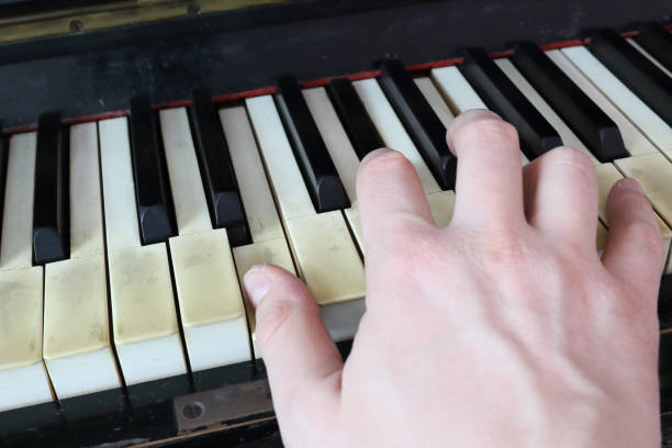 istock A right hand playing a E (MI) major chord on an old black piano with yellowed cracked keys, pressing the E (MI), G# diesis (SOL#), B (SI) notes 1088388978