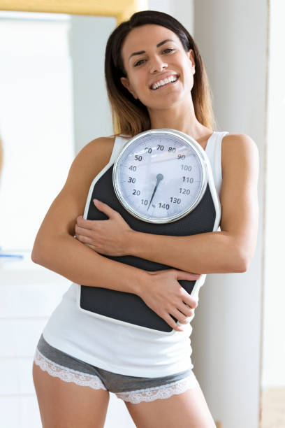 istock Happiness young woman holding weigh scale while looking at camera at home. 1088392242