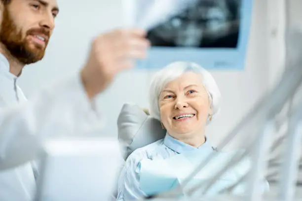 Happy elder woman during the consultation with handsome dentist showing panoramic x-ray in the dental office