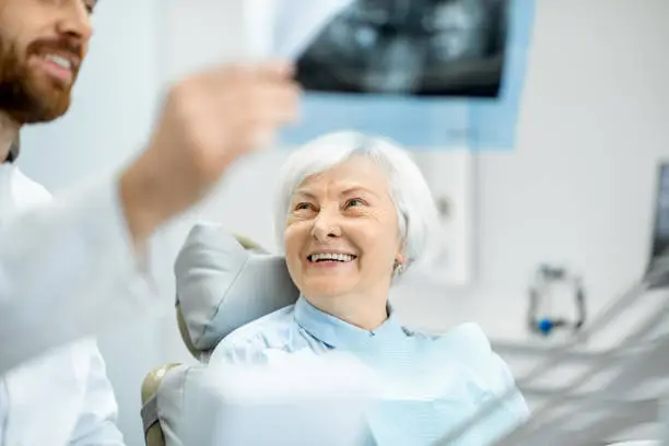 Happy elder woman during the consultation with handsome dentist showing panoramic x-ray in the dental office