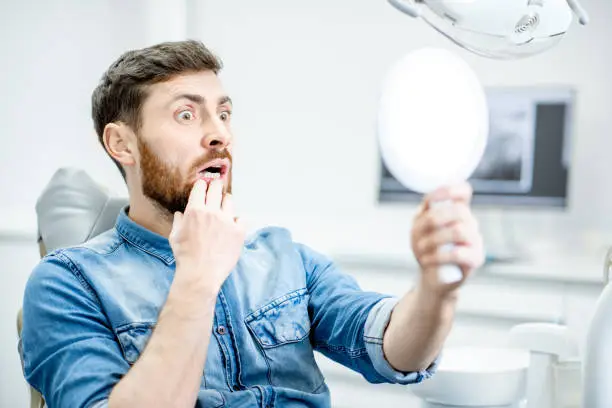 Portrait of a man worried with his teeth looking on the mirror in the dental office