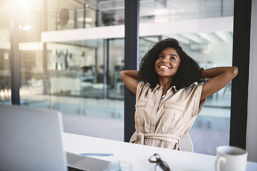 Shot of a happy young businesswoman relaxing at her desk in a modern office