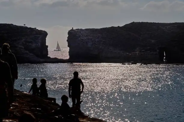 A ship sails by in the evening sunlight as holidaymakers are silhouetted in the foreground