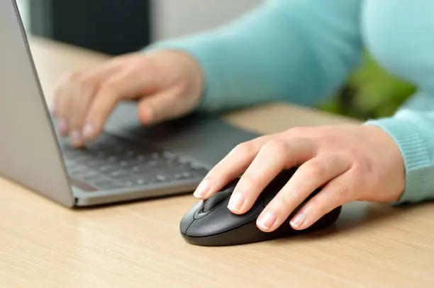 Close up of woman hands working with a laptop and a mouse at home