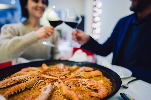 Young couple giving a celebratory toast in restaurant.Fresh seafood paella with shrimps served on the table.