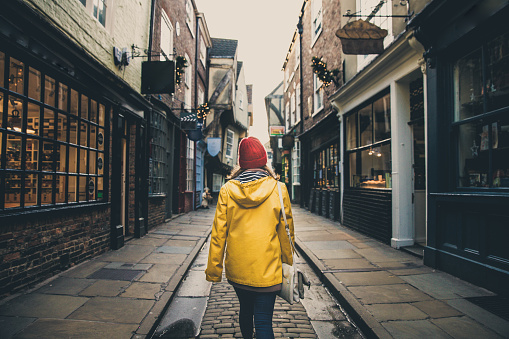 A rear view of a female in a bright yellow coat walking along the historic street known as The Shambles in York, UK which is a popular tourist destination in this Yorkshire city.