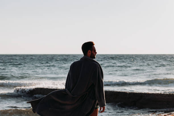 istock Young man in a bathrobe on the beach in sunset 1088451896