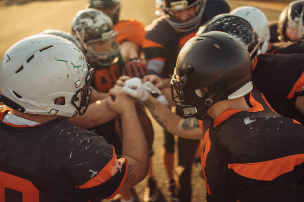 us-amerikanischer american-football-spieler kauern - köpfe zusammenstecken stock-fotos und bilder