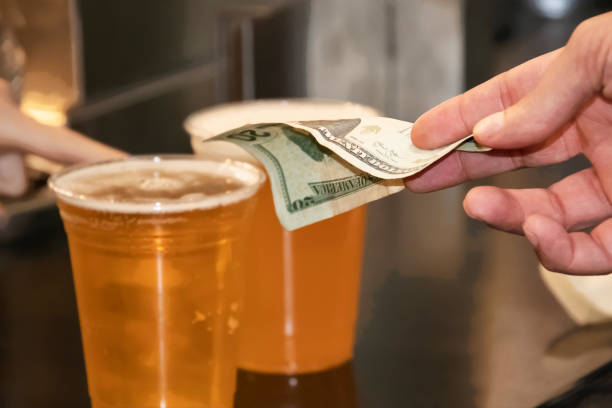 Mans hand paying for two plastic cups of beer with a USD twenty dollar bill stock photo