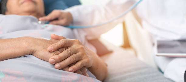 Hospitalized elderly patient, senior old aging woman laying on bed with cardiologist doctor or physician examining cardiological heart health, checking pulse in hospital clinic exam room Hospitalized elderly patient, senior old aging woman laying on bed with cardiologist doctor or physician examining cardiological heart health, checking pulse in hospital clinic exam room one senior woman only stock pictures, royalty-free photos & images