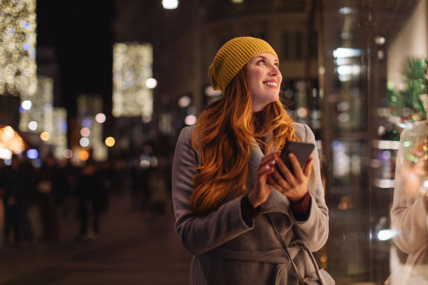 Women looking at store window Women walking and using smartphone. window shopping at night stock pictures, royalty-free photos & images