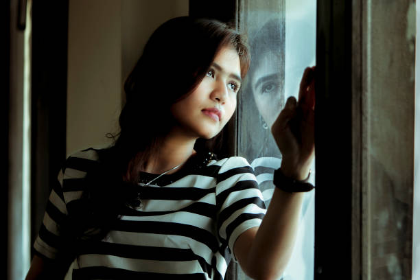 istock thoughtful asian girl standing at window 1088609674