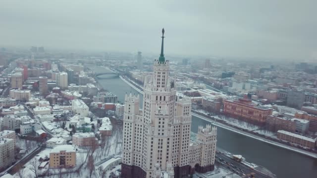 Aerial footage of  Moscow sights, Stalin's skyscraper near Moscow river in winter. There are snowy roofs of houses and driving cars.