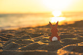 Creative easter photo of red paper bunny on the sand on the beach at sunset. Concept of Easter celebrations in tropical countries.