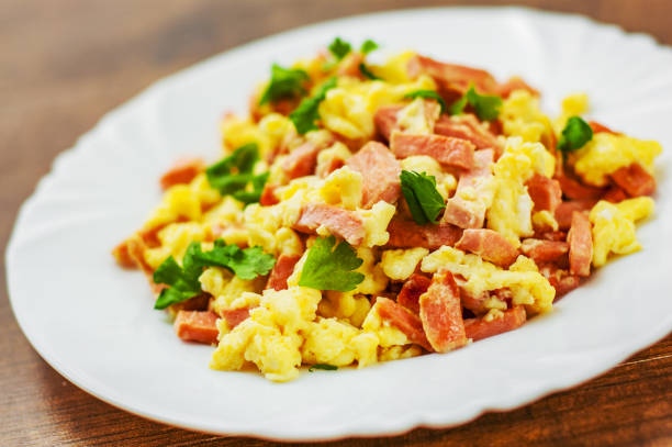 scrambled eggs with ham and cheese in white plate on wooden table background