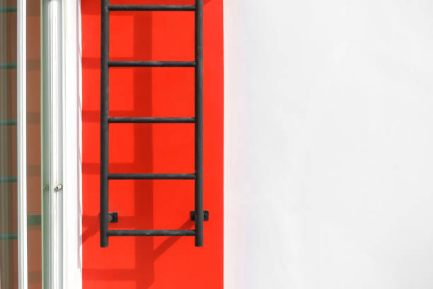 black fixed ladder with shadow on red wall and space of white concrete wall