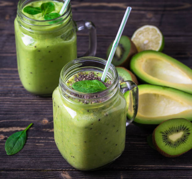 istock Green smoothie on dark background with avocado, spinach, lemon and kiwi on the right side. 1088746880