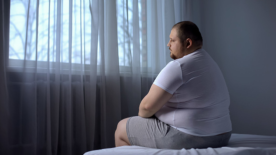 Depresión hombre gordo sentado en la cama en su casa, preocupado por sobrepeso, inseguridades photo