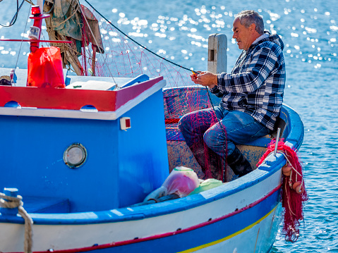 Procida Island in the Campania region of Italy on October 26, 2017: Elderly fisherman  mending traditional fishing nets by hand on Procida Island harbor
